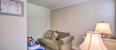 A cozy room with a green sofa, a small blue chair, a lamp, and a framed picture on the wall.
