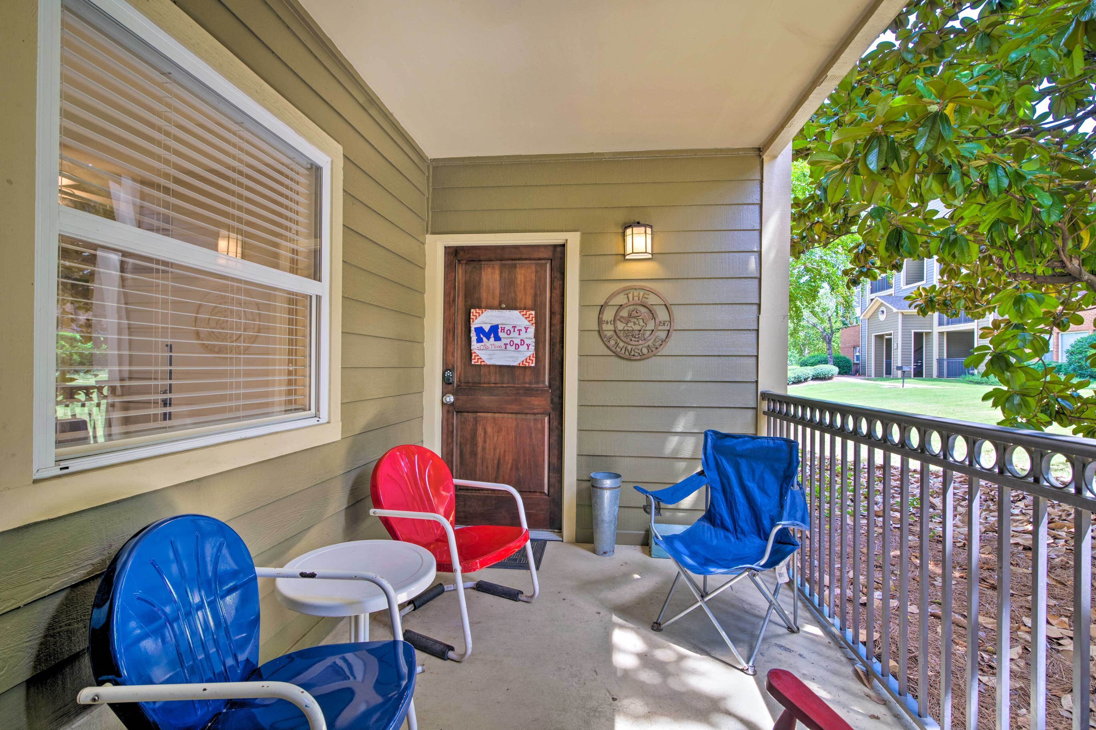 A porch with two blue folding chairs, a red folding chair, and a small white table.