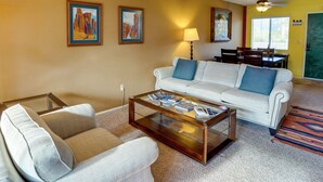 A living room with a white sofa, a glass coffee table, and two armchairs. There are paintings on the wall, a lamp, and a dining area in the background. - Borrego Springs Vacation Rental: Patio & Gas Grill (Borrego Springs)