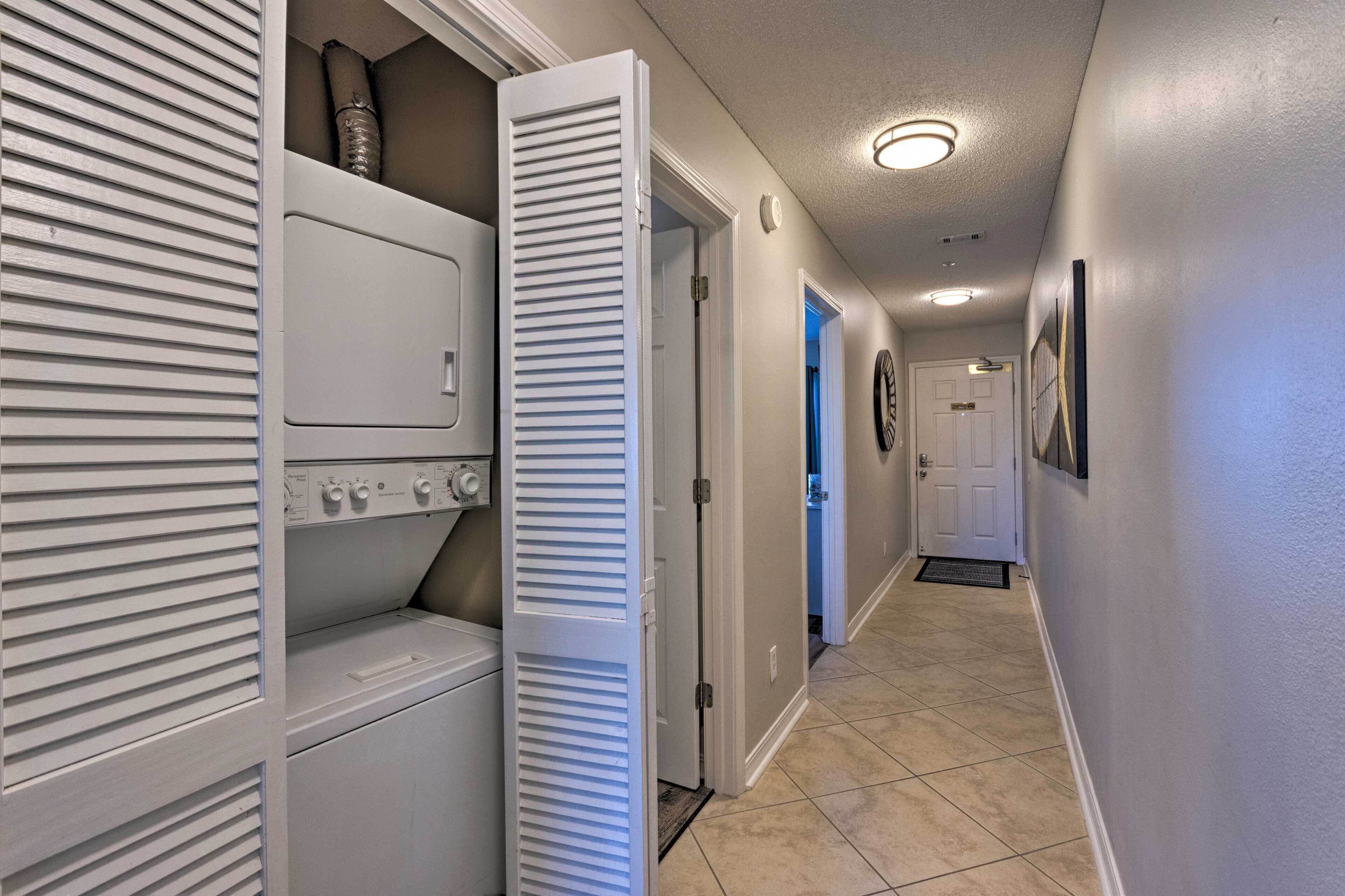 A laundry room with a washer and dryer, a door leading to another room, and a hallway with a door at the end.