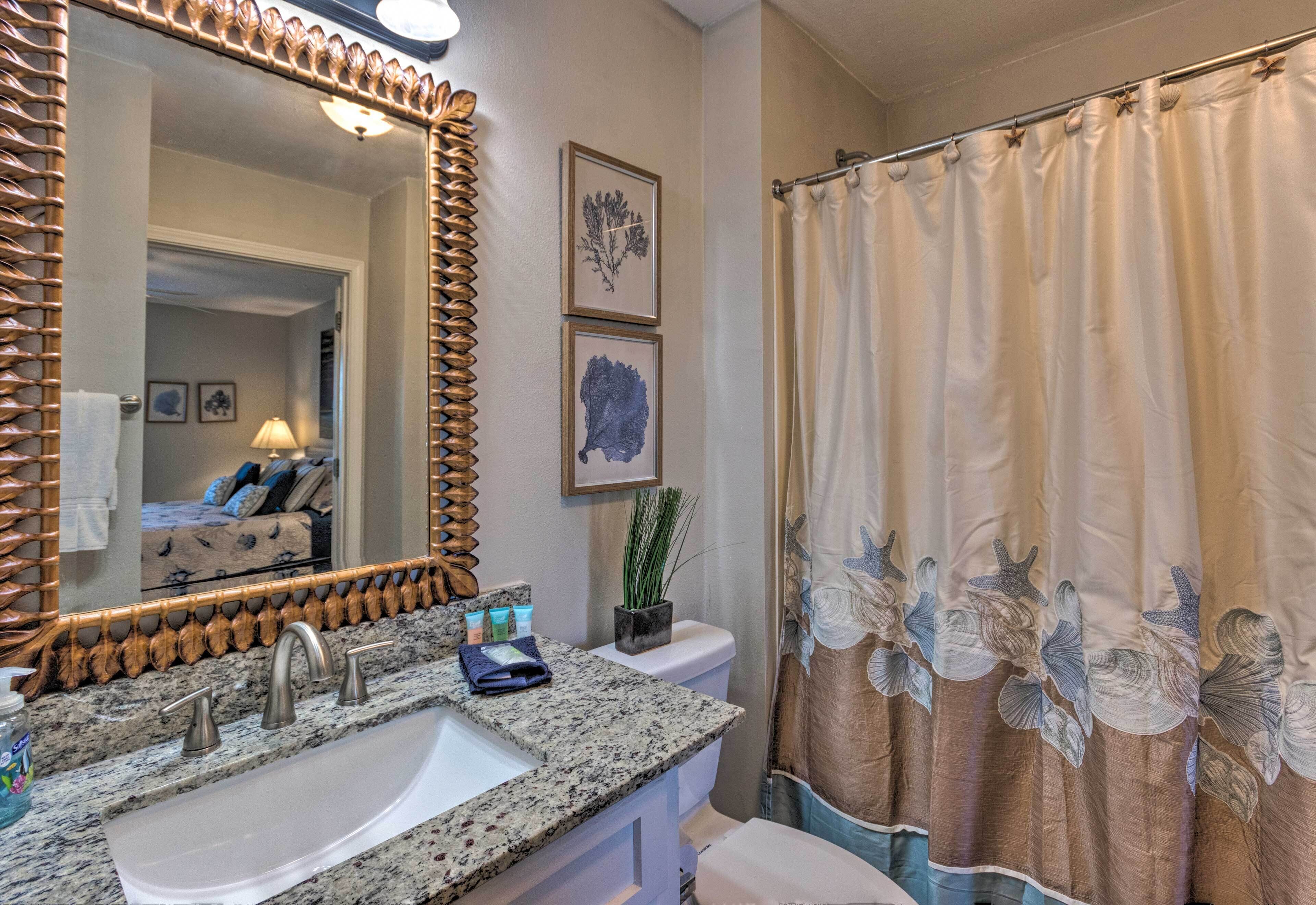 A bathroom with a granite countertop sink, a large mirror, and a shower curtain with a sea creature design.