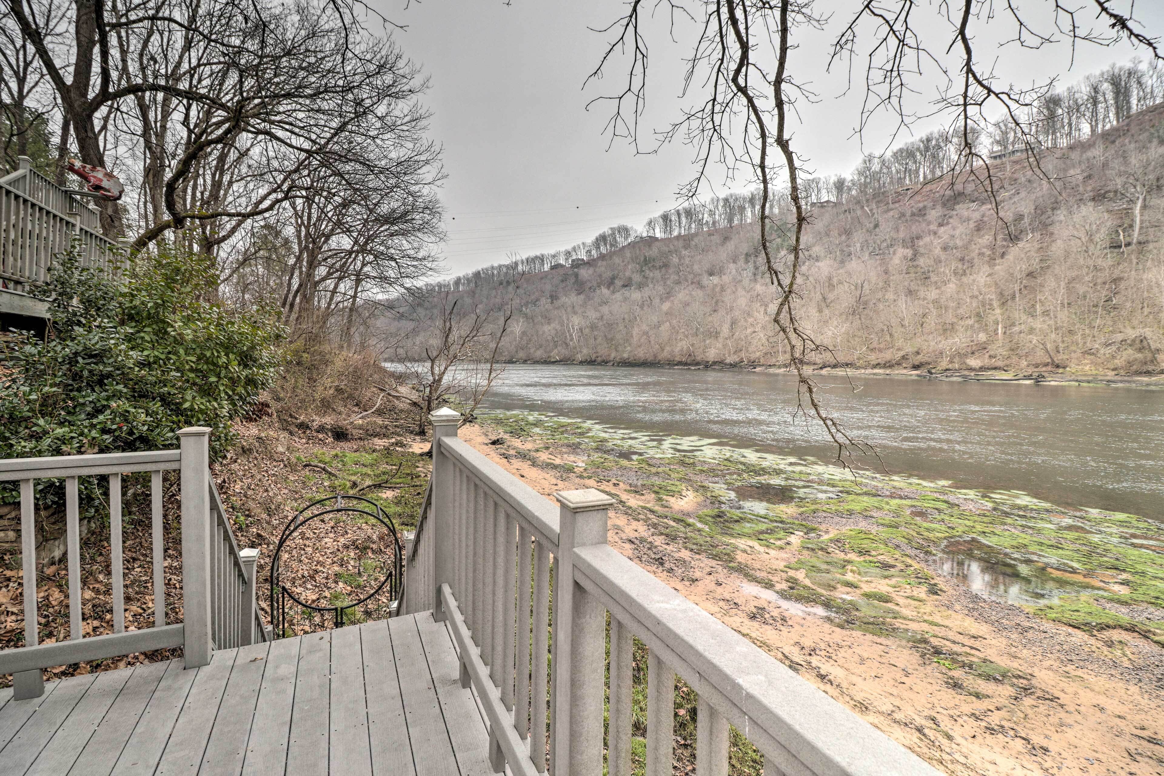 A wooden deck overlooking a river with sparse vegetation and a forested hillside.