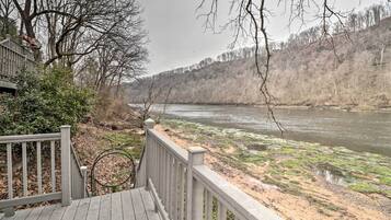 A wooden deck overlooking a river with sparse vegetation and a forested hillside.