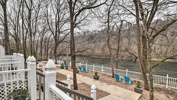 A deck with a white railing, potted plants, and blue chairs overlooking a river. - Riverside Studio: Trophy Trout Fishing On-site (Lakeview)