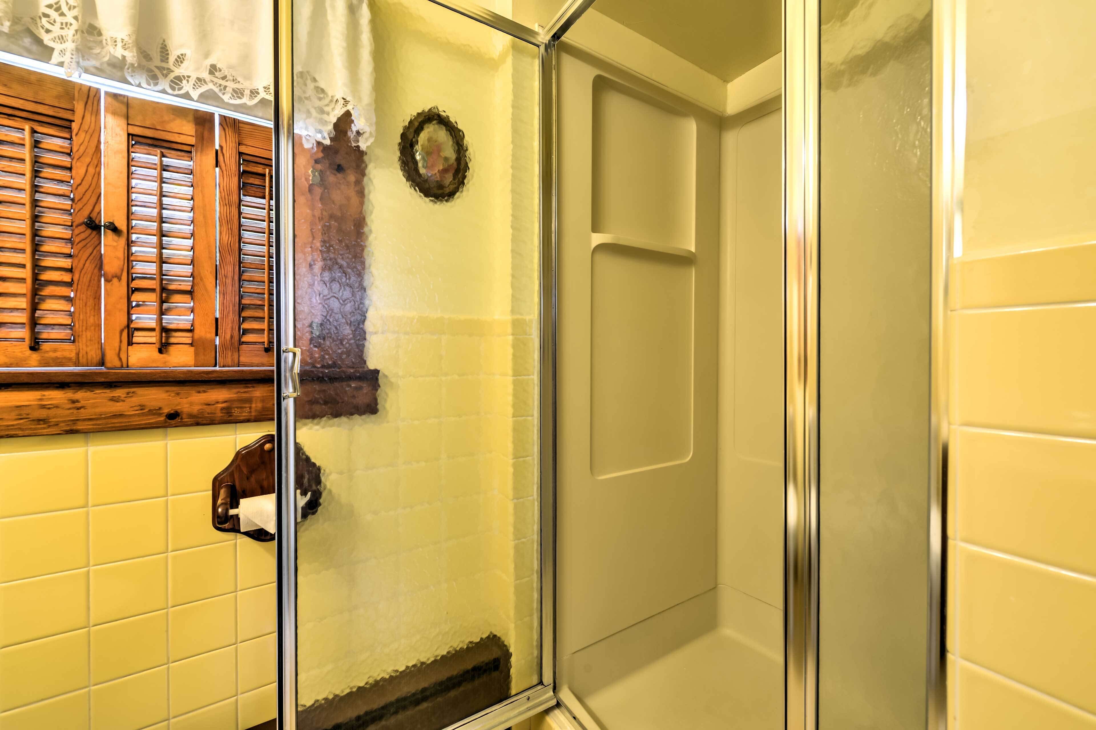 A bathroom with yellow tiles, a wooden window shutter, a glass shower door, and a towel rack.