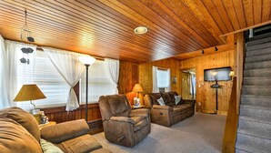 A cozy living room with wooden paneling, a sofa set, a recliner, a lamp, and a television.
