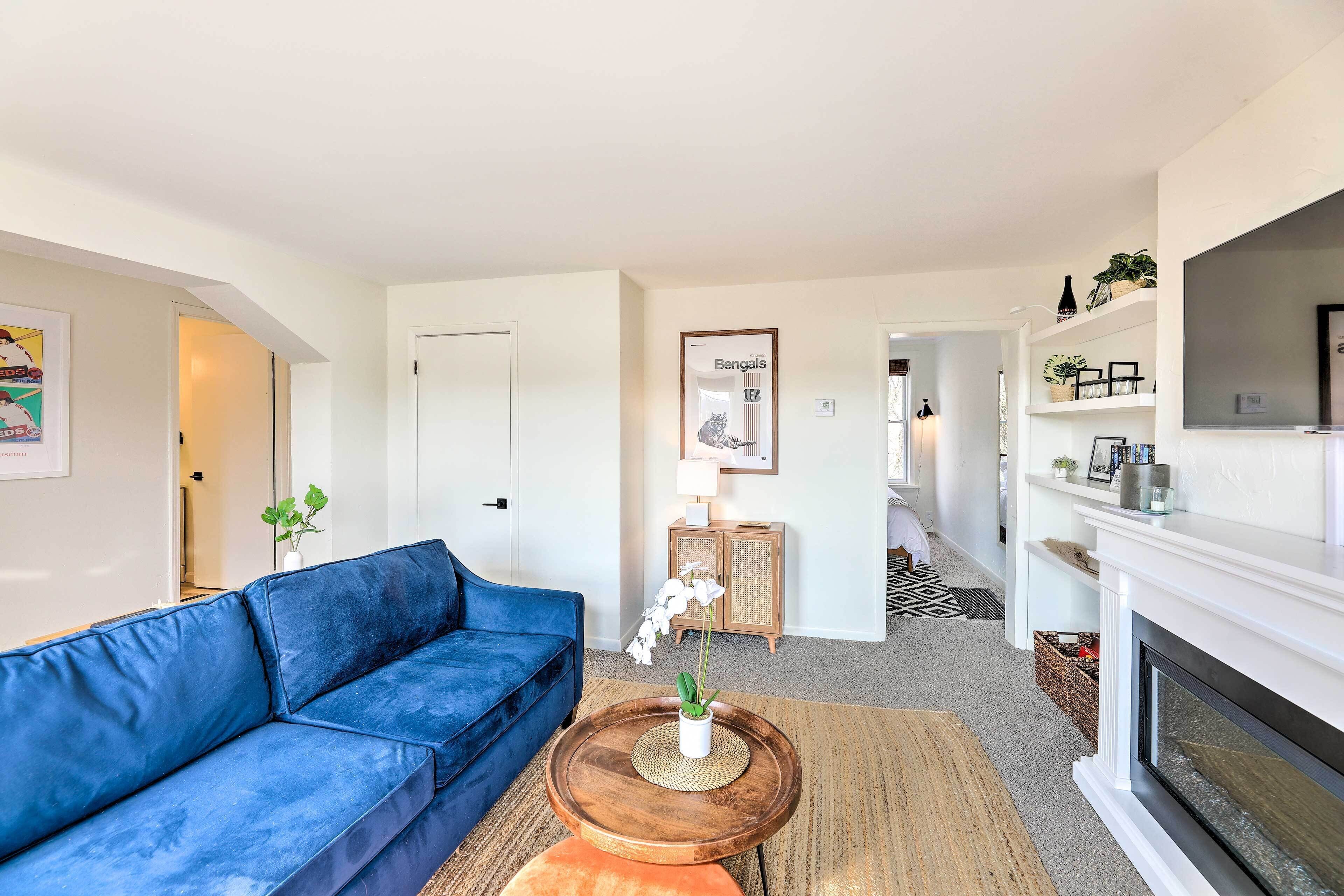 Ein Wohnzimmer mit einem blauen Sofa, einem Couchtisch aus Holz mit einer Pflanze, einem Kamin und einem gerahmten Bild an der Wand.