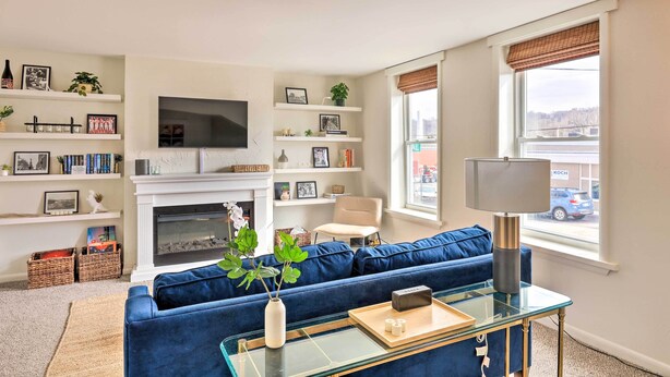 A living room with a blue sofa, a glass coffee table, a fireplace, and a TV mounted on the wall. - Cincinnati Vacation Rental: 6 Mi to Downtown! (Cincinnati)