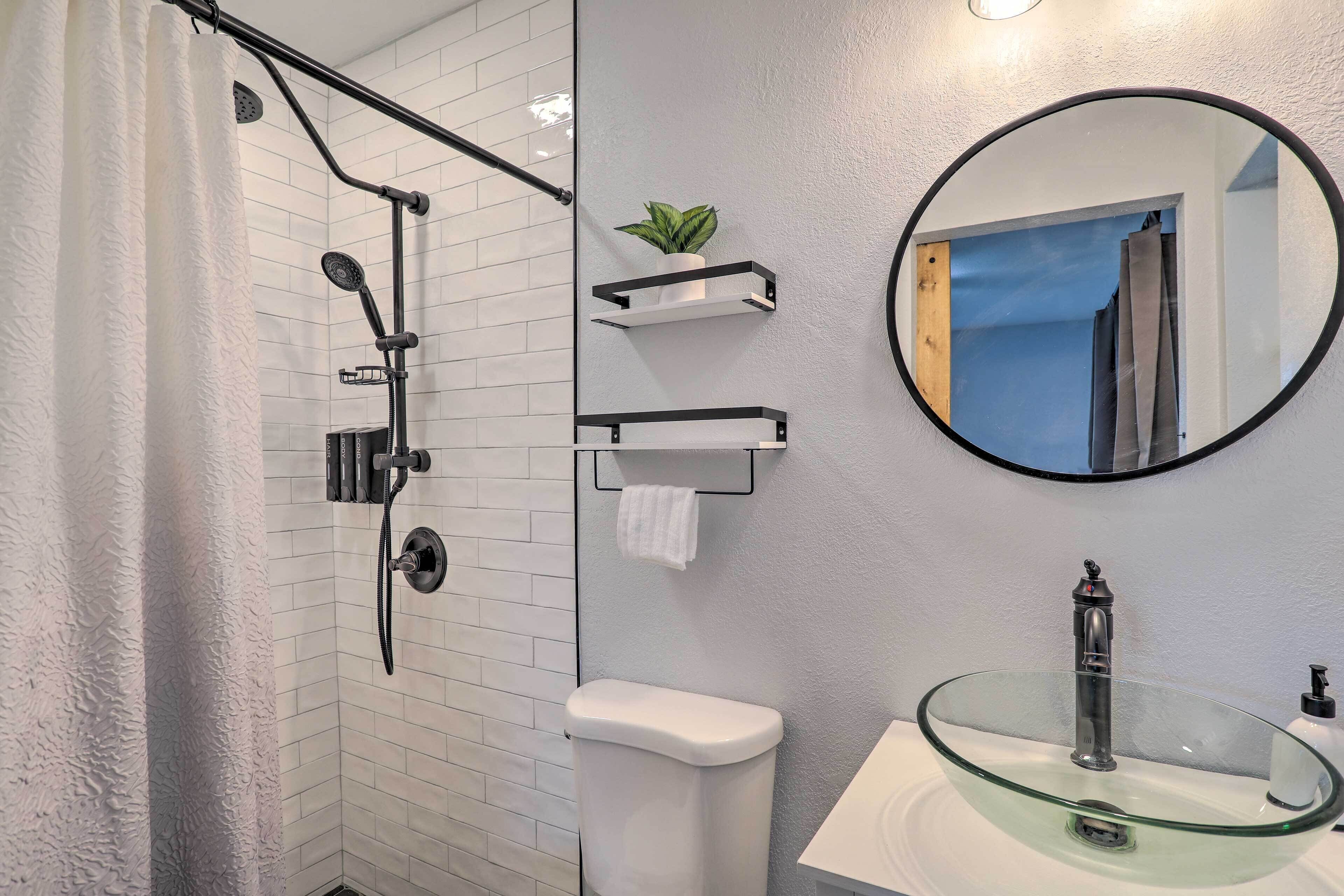 Une salle de bain moderne avec un lavabo en verre, une douche dotée d’un pommeau de douche à pluie et un porte-serviettes agrémenté d’une plante.