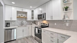 A modern kitchen with white cabinets, stainless steel appliances, and a marble countertop.