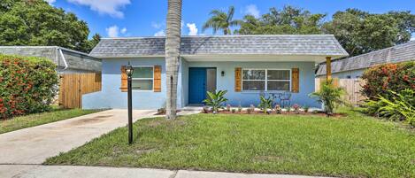 A single-story house with a blue exterior, a front door, and a small front yard with grass and plants.