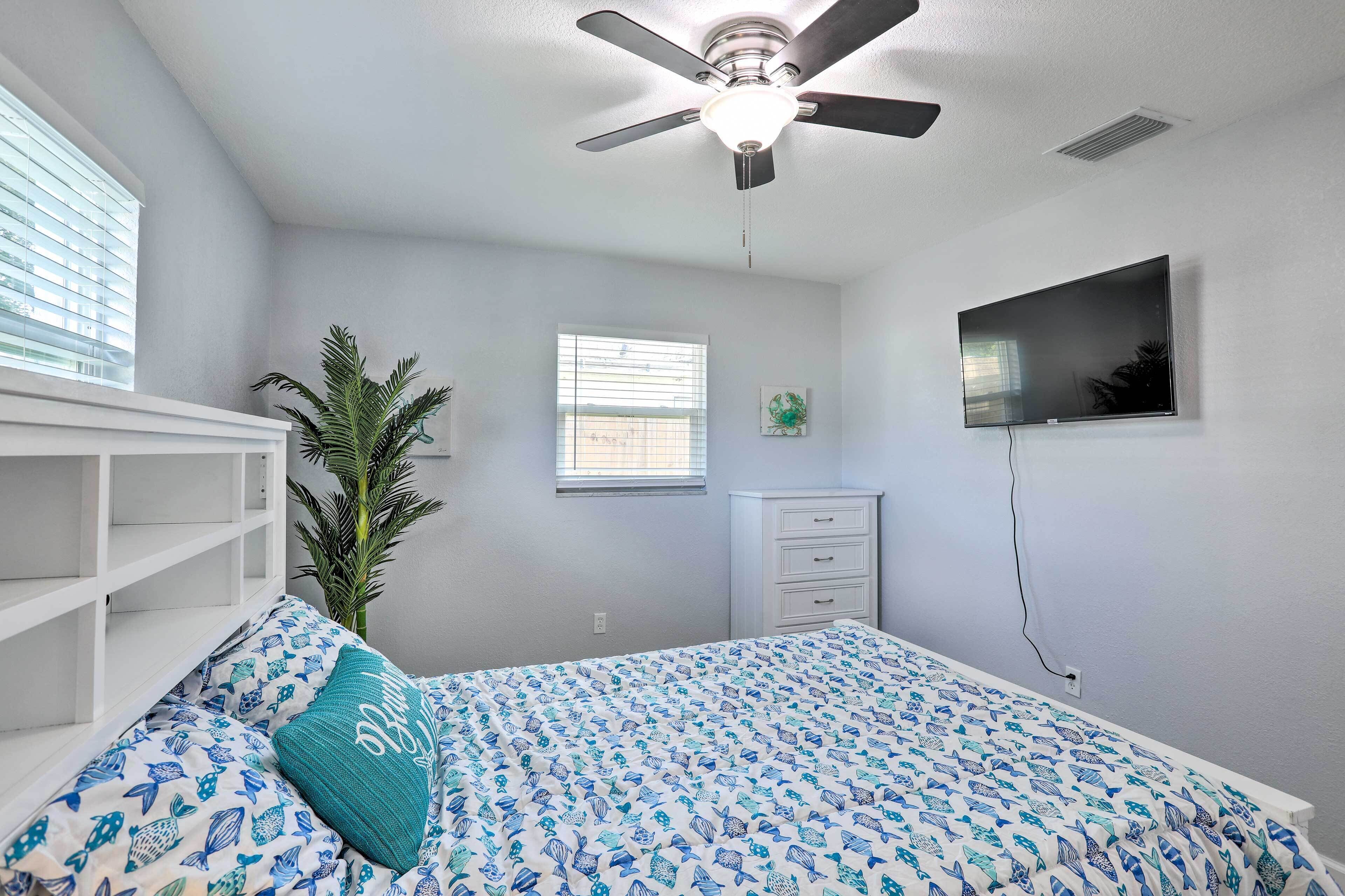 A bedroom with a bed, a ceiling fan, a TV, a dresser, and a window.