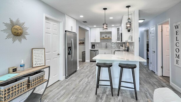 A modern kitchen with a central island, bar stools, a refrigerator, and a 'WELCOME' sign on the wall.