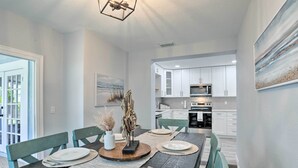 A dining area with a wooden table set for four, white chairs, and a view into the kitchen.