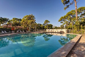 A clear swimming pool with lounge chairs and umbrellas, surrounded by trees and a building with a tiled roof. - Sarasota Villa w/ Pool Access ~ 4 Mi to Beach! (Sarasota)
