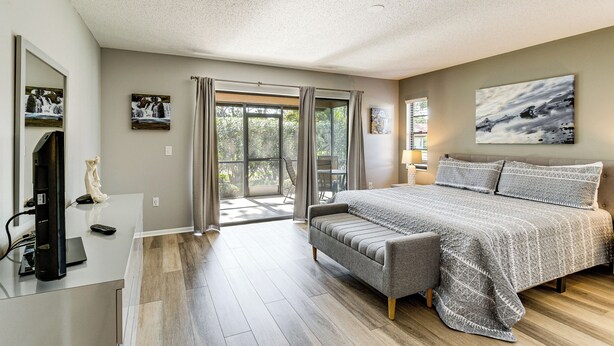 A bedroom with a large bed, a desk with a computer, and a view of the outdoors.