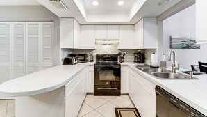 A modern kitchen with white cabinetry, a built-in oven, a dishwasher, and a large island with a sink.