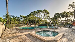 A pool area with two pools, lounge chairs, and a brick patio.