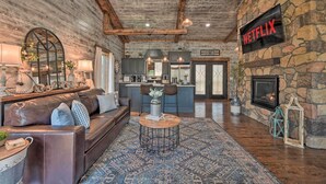 A cozy living room with a stone fireplace, a Netflix sign, and a modern kitchen in the background.