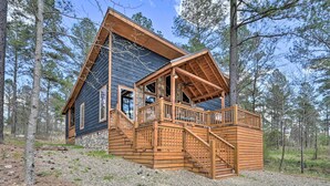 A cabin with a stone foundation, wooden exterior, and a wooden deck with stairs leading to a porch.