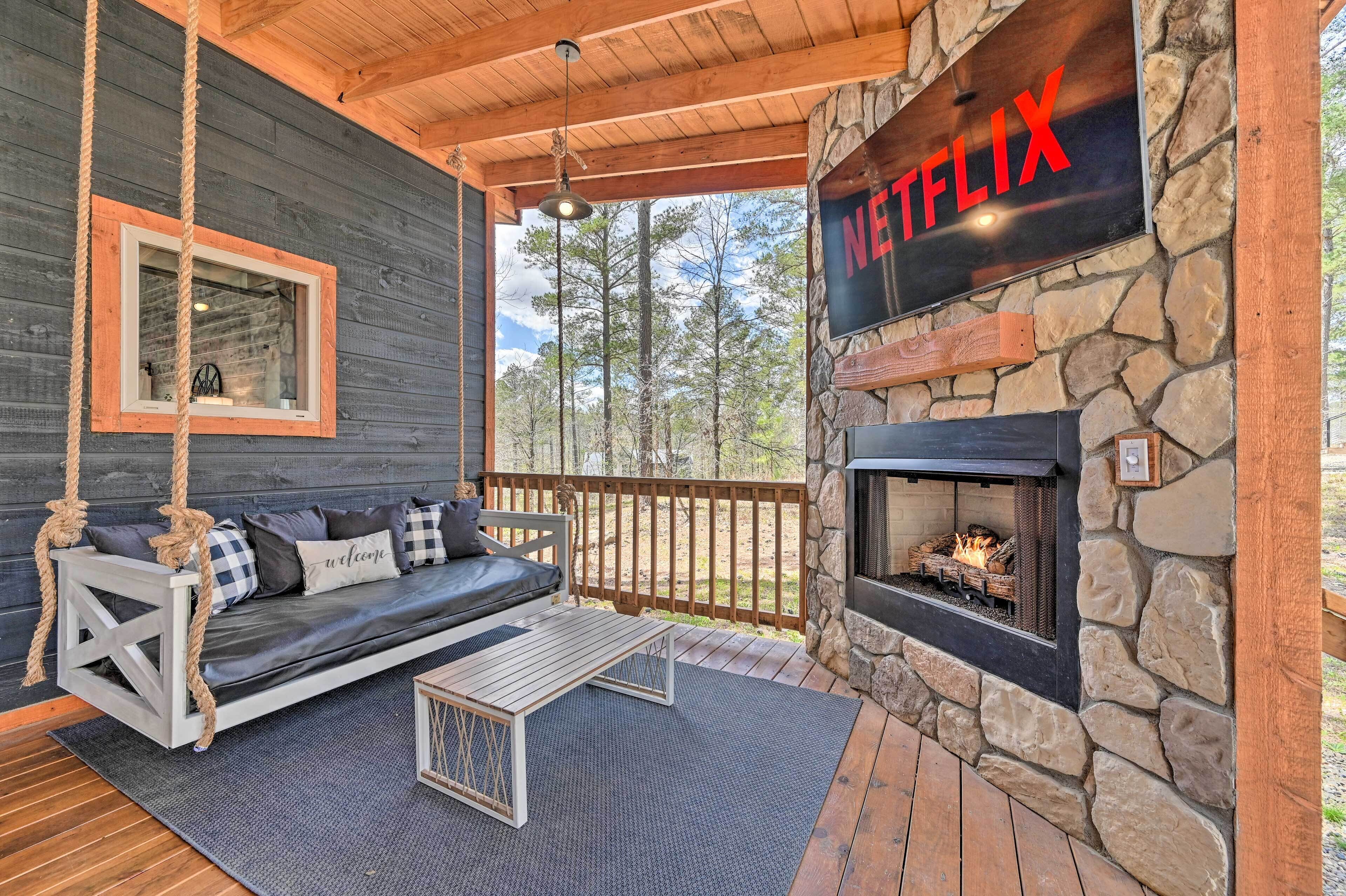 A cozy outdoor seating area with a swing, a stone fireplace, and a Netflix sign.