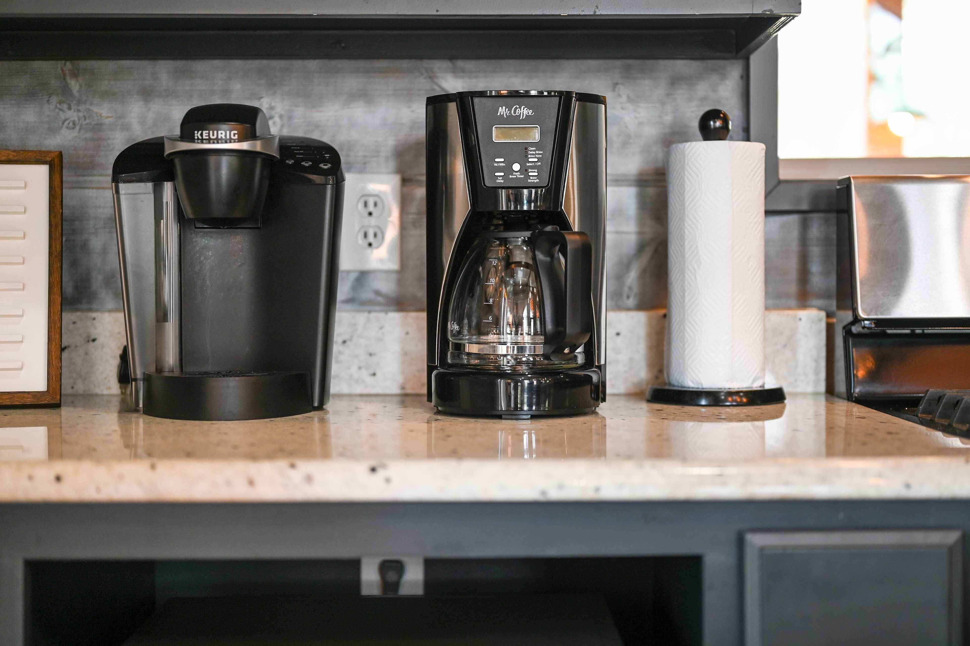 Una encimera de cocina con dos cafeteras y un rollo de toallas de papel.