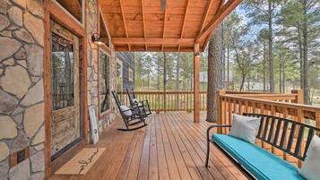 A wooden deck with a rocking chair and a bench, a stone wall, and a view of the forest.