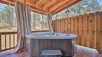 A hot tub on a wooden deck with a wooden fence and trees in the background.