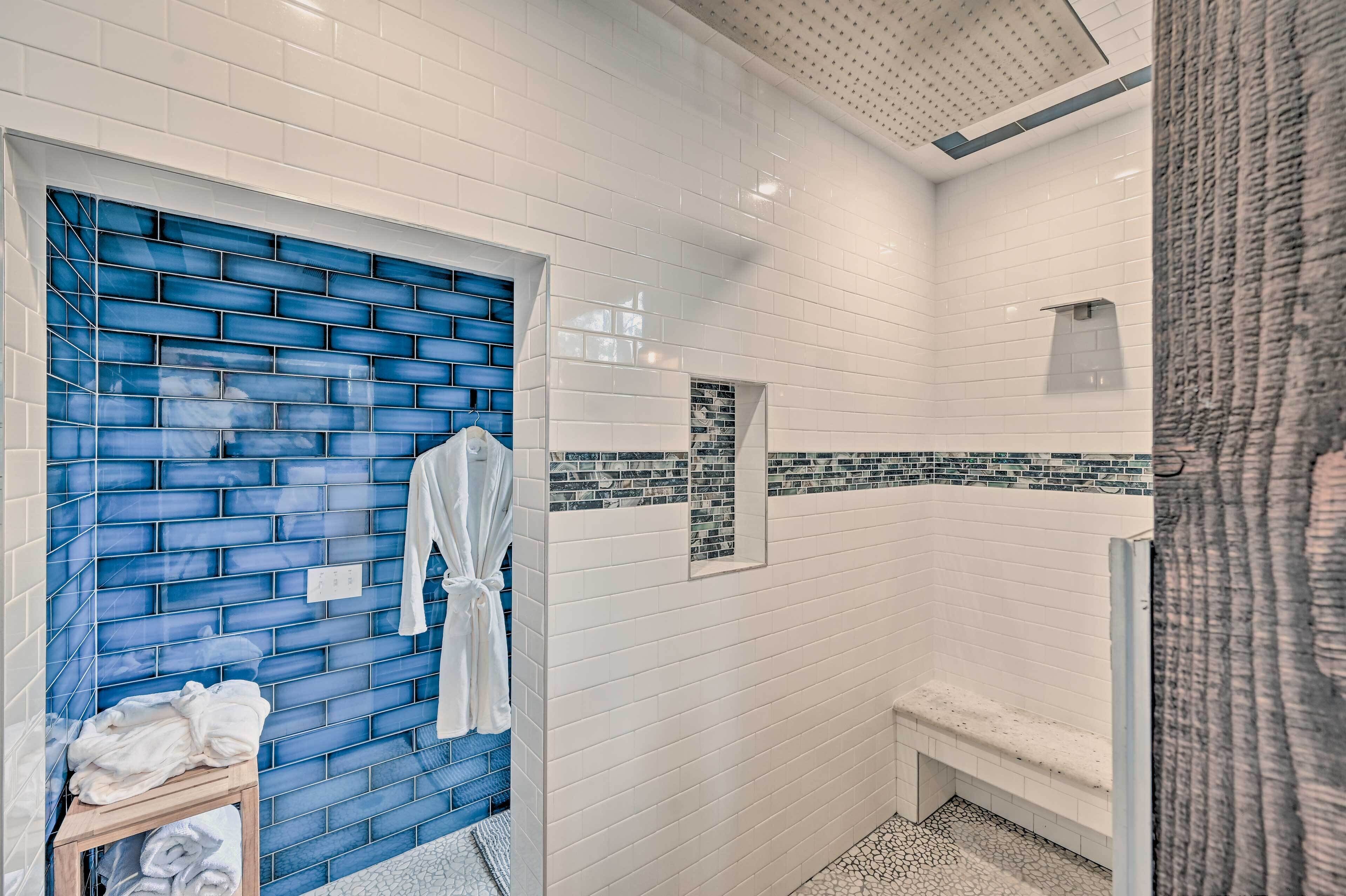 A bathroom with white tiled walls, a blue-tiled accent wall, a bench, and a towel rack.