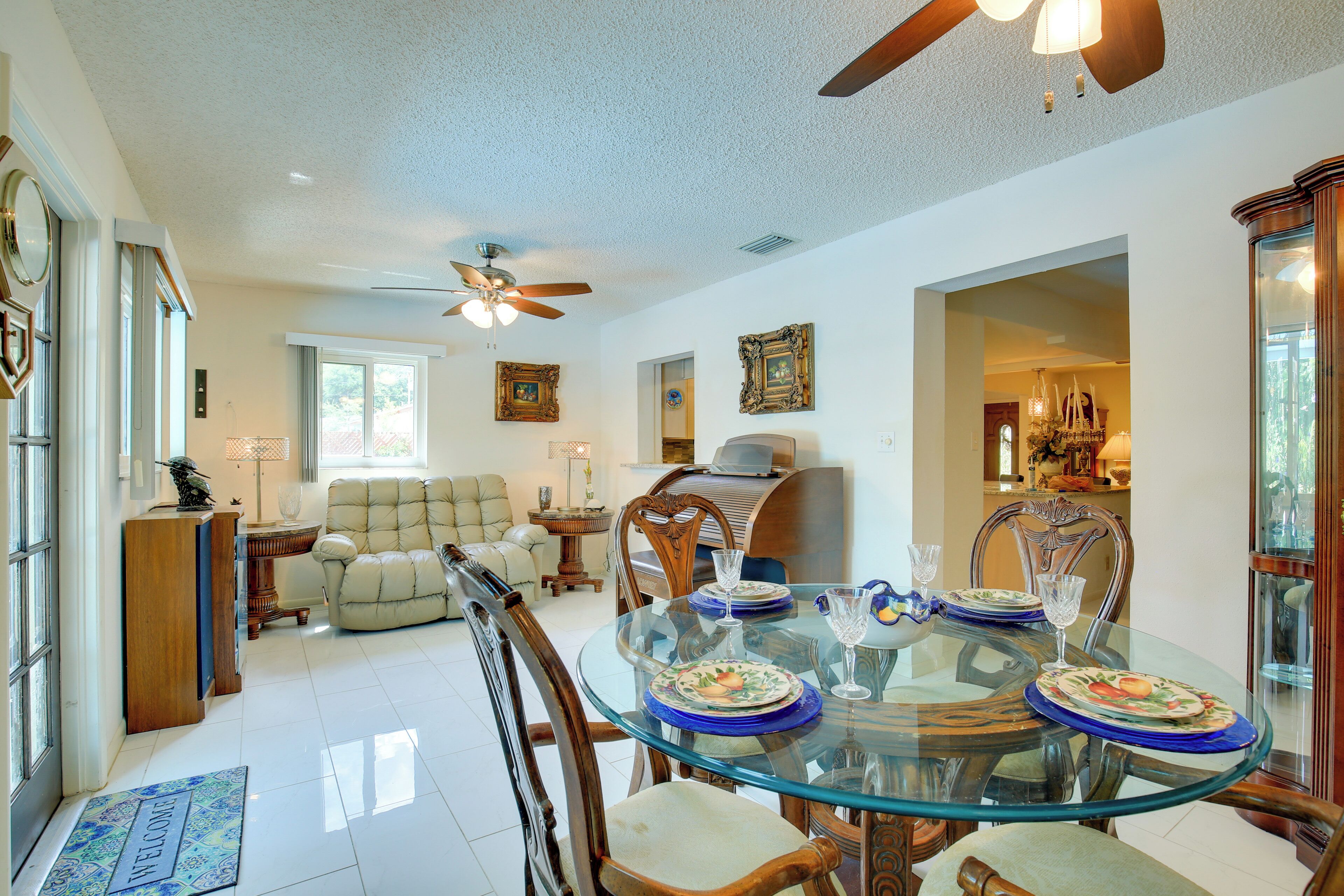 A spacious dining area with a glass table, wooden chairs, and a ceiling fan.