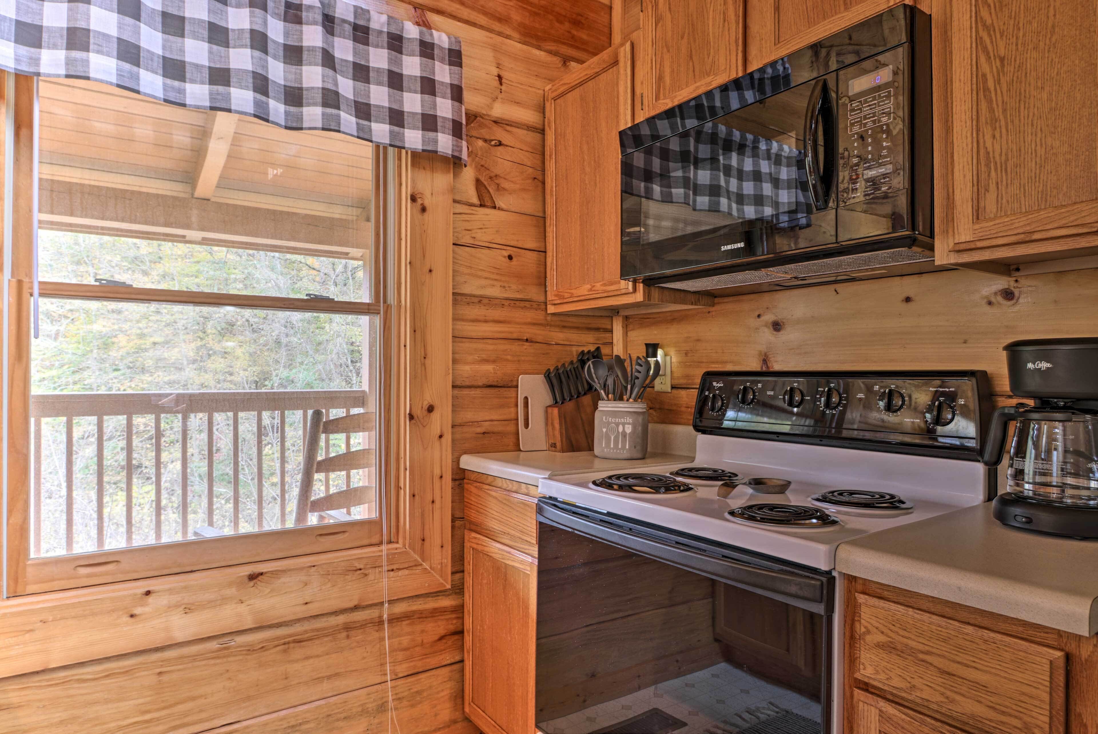 Cocina de cabaña de madera con estufa, microondas y ventana con vistas a una terraza.
