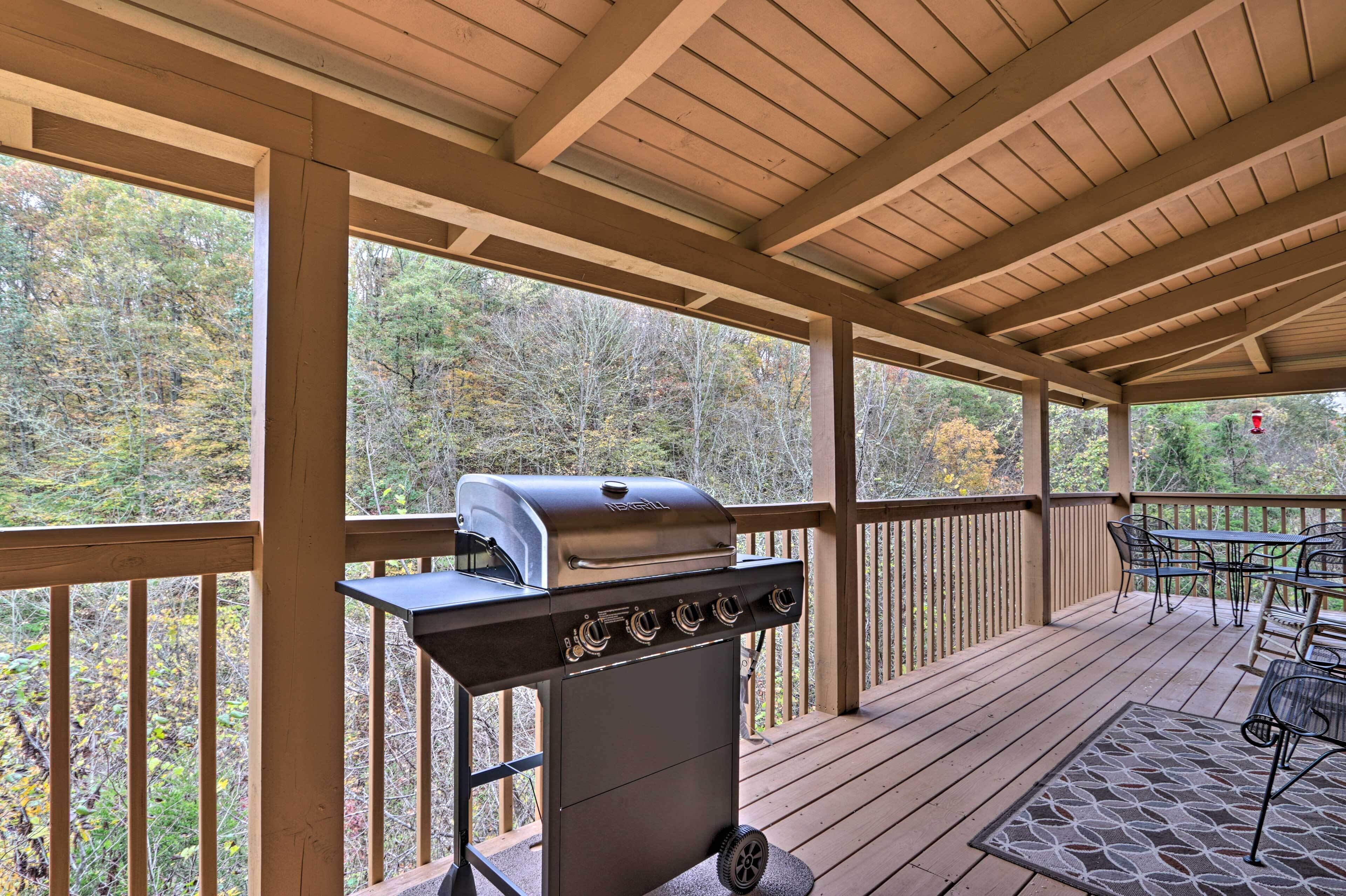 A covered outdoor deck with a grill, a table with chairs, and a view of trees.