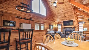 A wooden cabin interior with a dining area, kitchen, and fireplace.