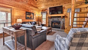 A cozy log cabin interior with a fireplace, a leather sofa, a television, and a stone fireplace surround.