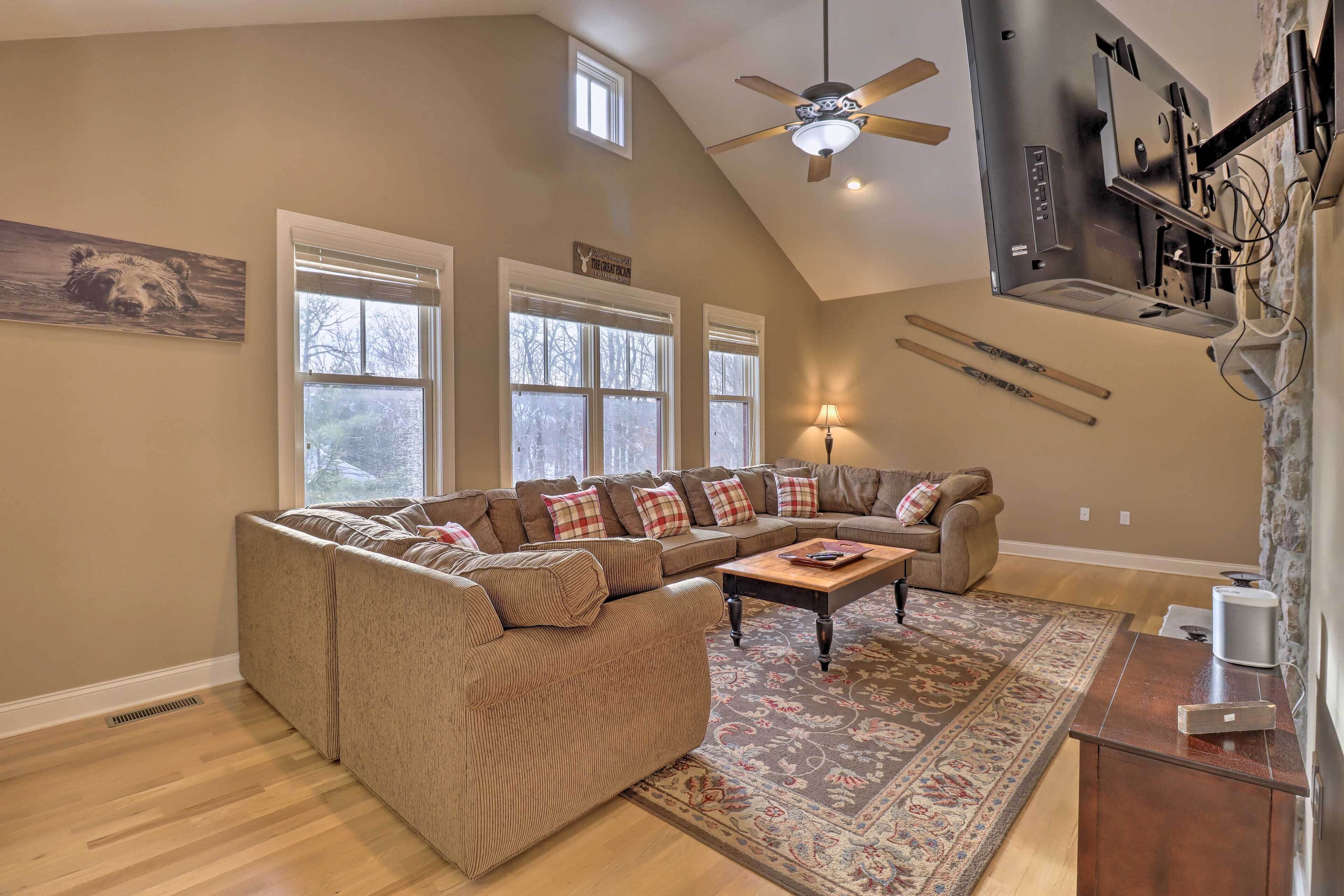 A living room with a sectional sofa, a coffee table, a patterned rug, a ceiling fan, and a fireplace.