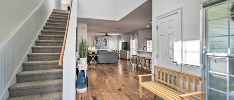 A spacious living area with a wooden bench, a staircase, and a view of the kitchen.