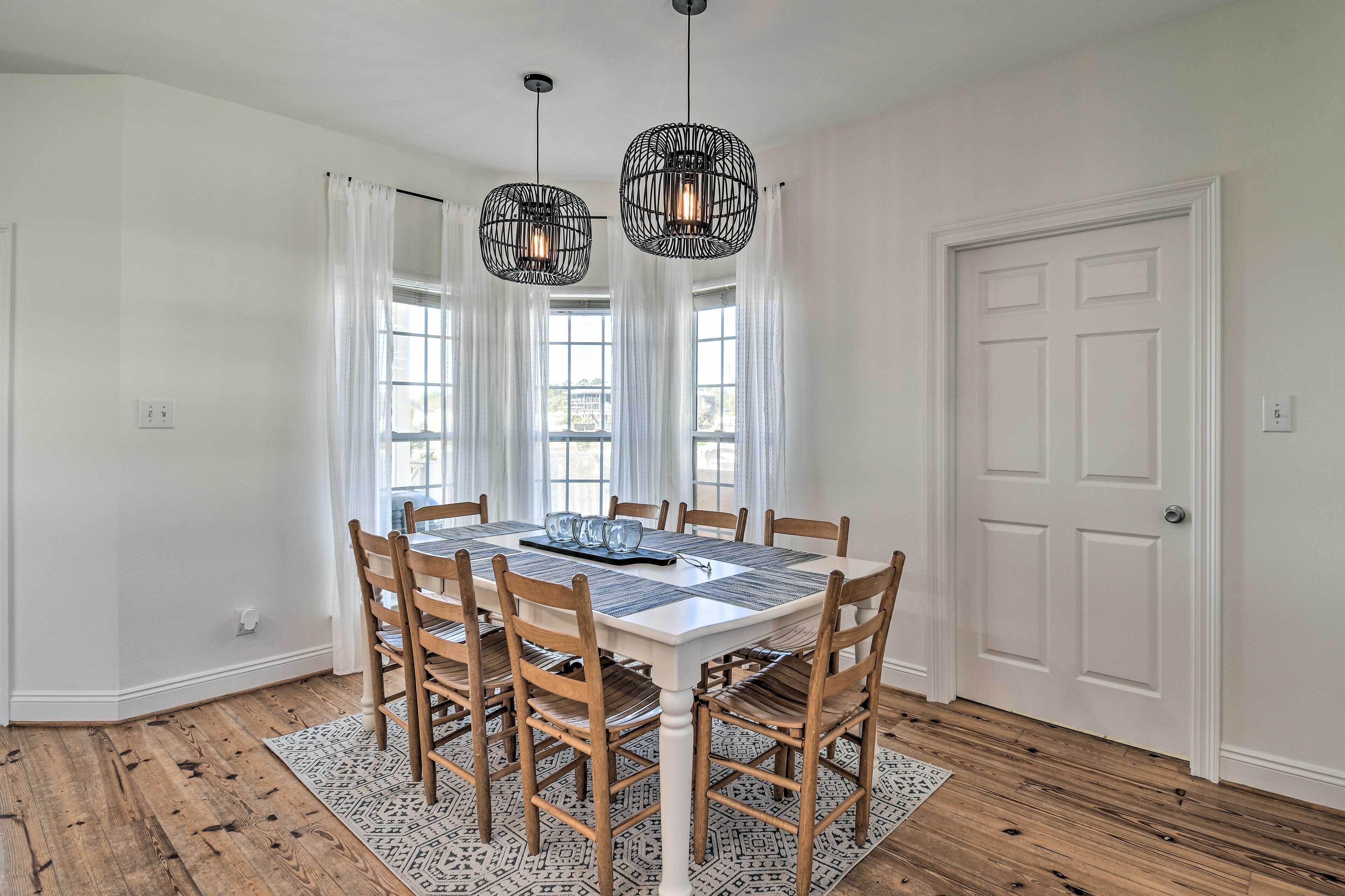 A dining room with a white table, wooden chairs, and black hanging lights.