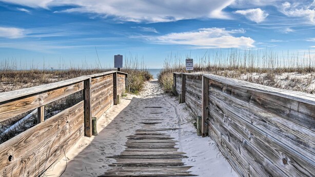 Un paseo marítimo de madera que lleva a una playa, con un cartel que indica una reserva natural.