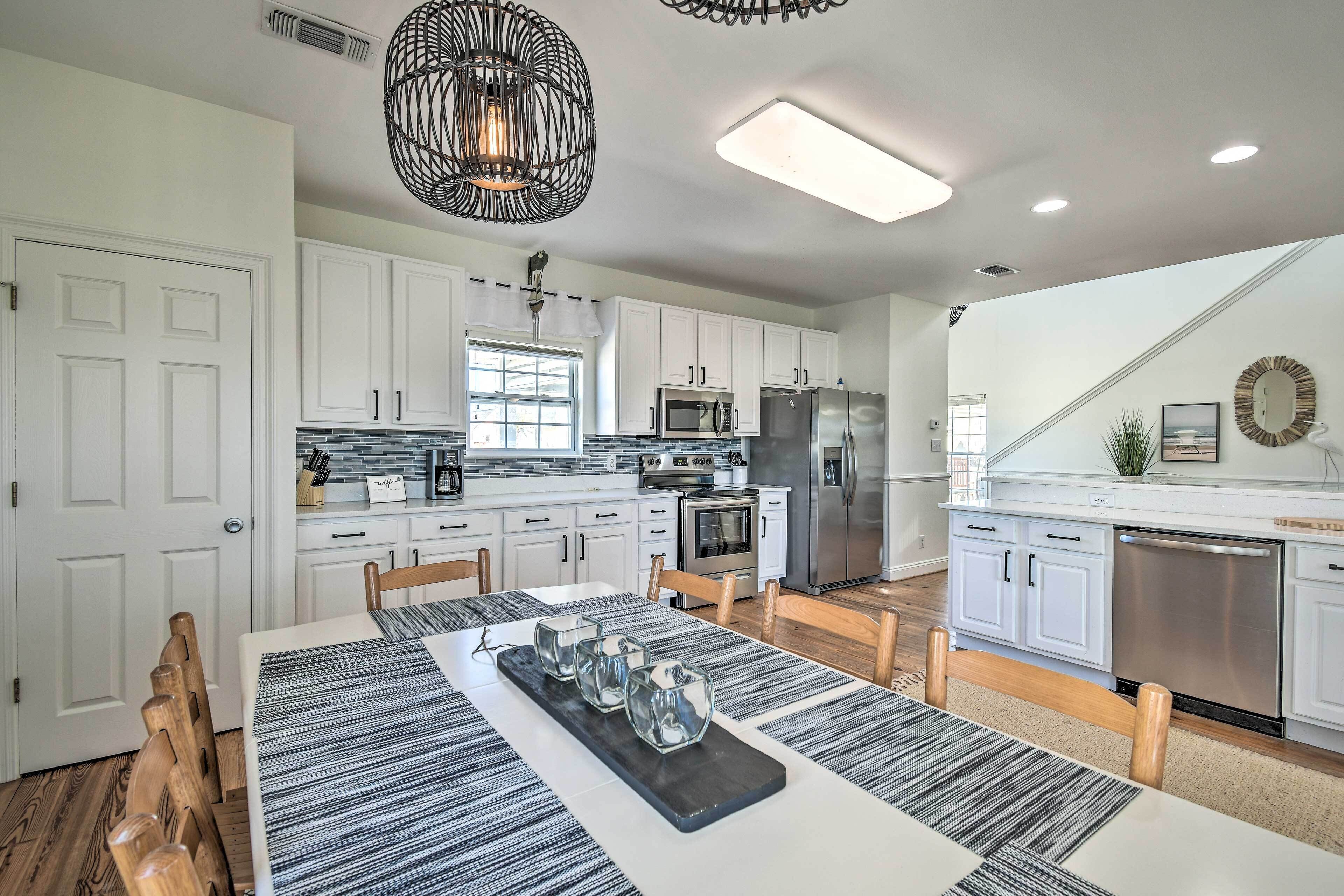 A modern kitchen with white cabinets, stainless steel appliances, and a dining area with a striped table runner and glassware.