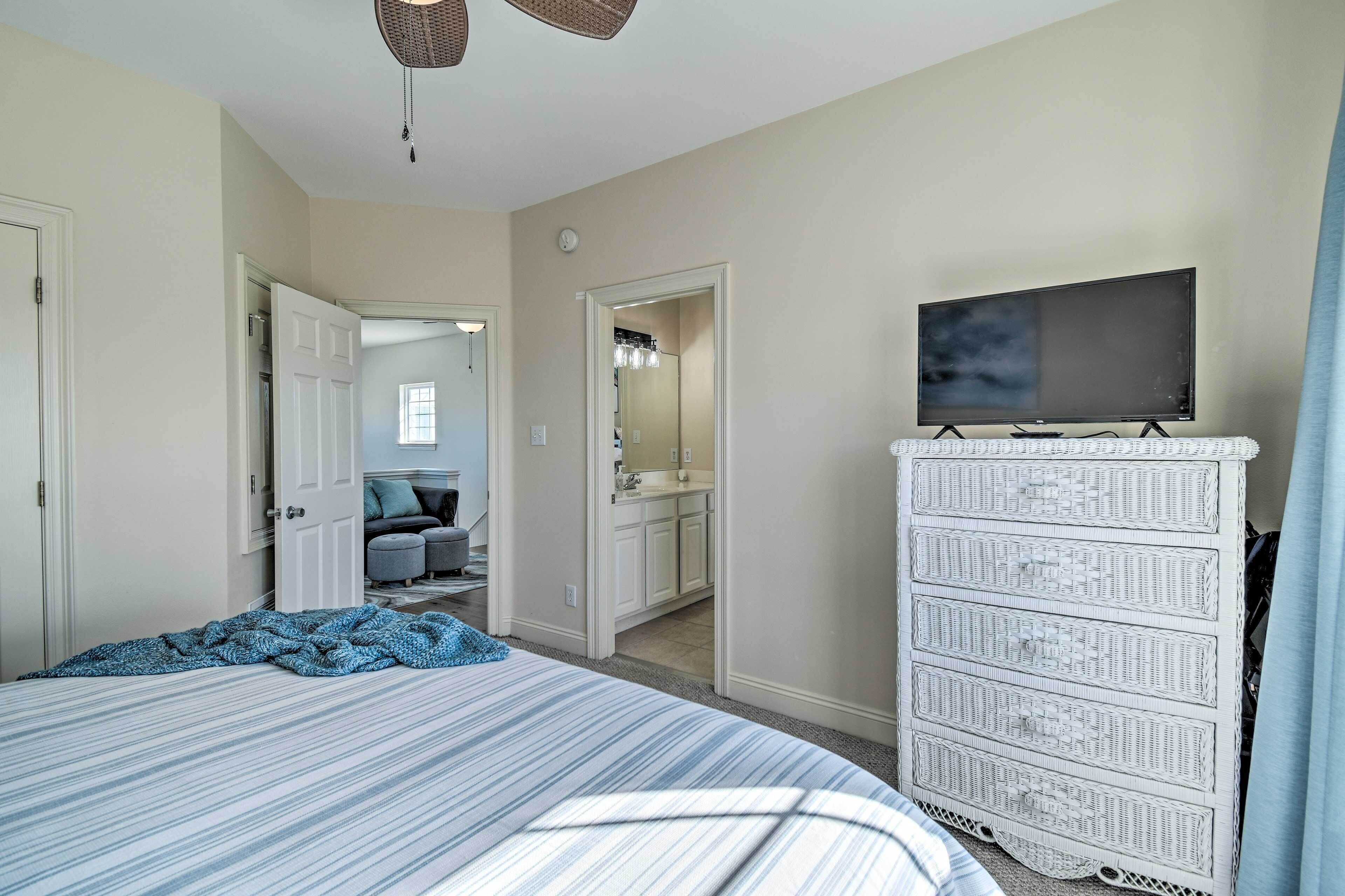 Une chambre à coucher comprenant un lit, une commode, un téléviseur et un couloir menant à la salle de bain.