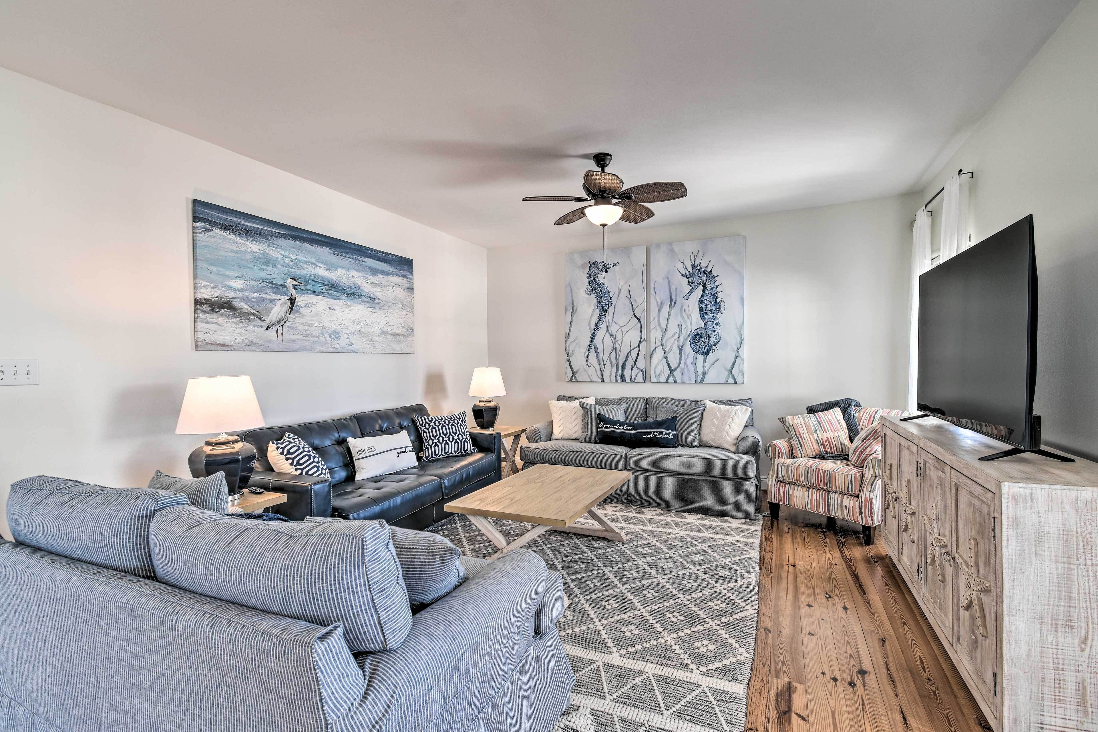 A modern living room with a sofa, coffee table, and TV. There is a ceiling fan and artwork on the walls.