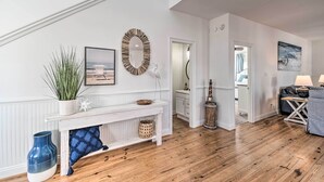 Amplia sala de estar con piso de madera, paredes blancas y una consola blanca con objetos decorativos.