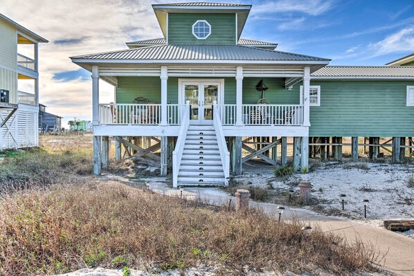 A green wooden house with a white porch and a staircase leading to the entrance.