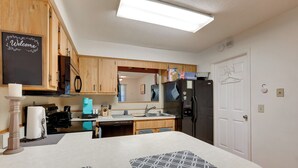 A modern kitchen with wooden cabinets, a black refrigerator, a sink, and a welcome sign on the wall. - Ocala Home < 7 Mi to World Equestrian Center! (Ocala)