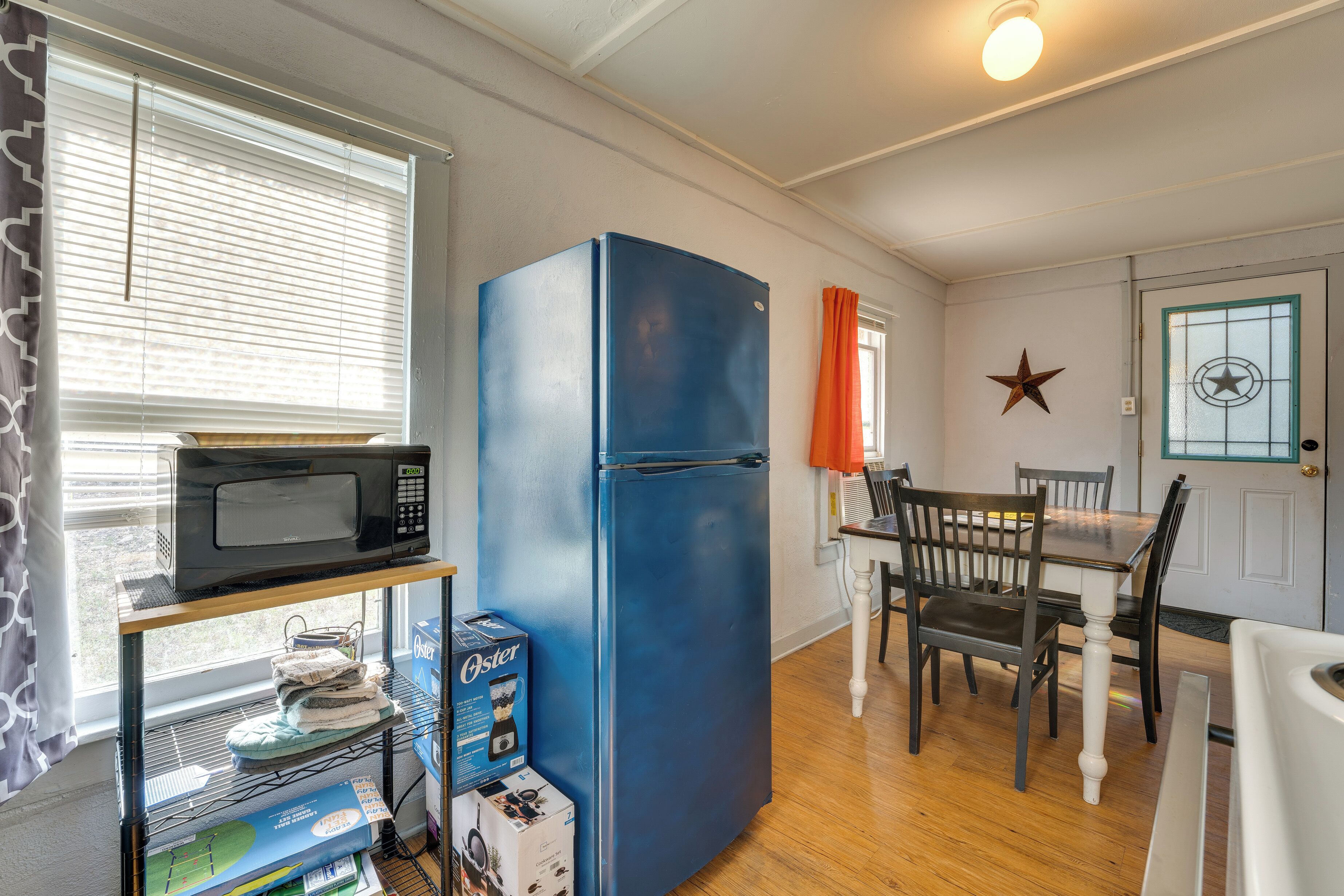 A compact kitchen with a blue refrigerator, a microwave on a shelf, and a dining table with chairs.