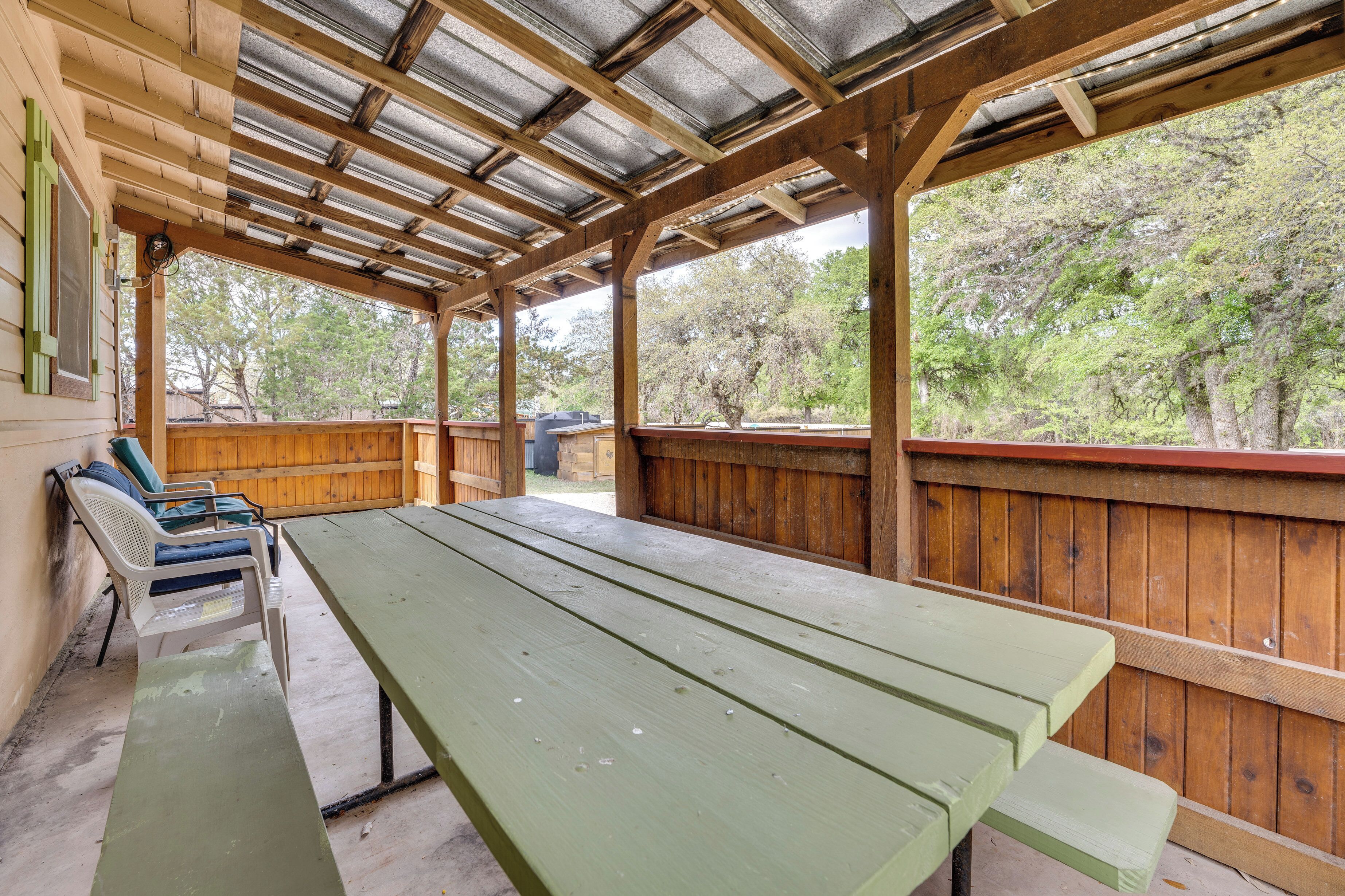 A covered picnic area with wooden benches and a table, surrounded by a wooden fence and trees.