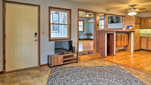 A spacious living area with a large TV, wooden cabinets, and a patterned rug. - Table Rock Lake House w/ Fire Pit: Steps to Water! (Branson West)