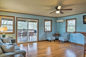A spacious living room with a wooden floor, a ceiling fan, and a sliding glass door leading to an outdoor patio. - Table Rock Lake House w/ Fire Pit: Steps to Water! (Branson West)