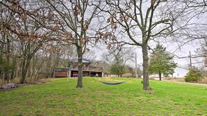 A grassy area with a hammock, trees, and a building with a covered porch in the background. - Table Rock Lake House w/ Fire Pit: Steps to Water! (Branson West)