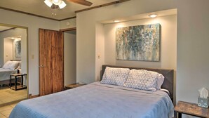 A bedroom with a bed, a ceiling fan, a wooden door, a painting, and a bedside table with a tissue box. - Table Rock Lake House w/ Fire Pit: Steps to Water! (Branson West)